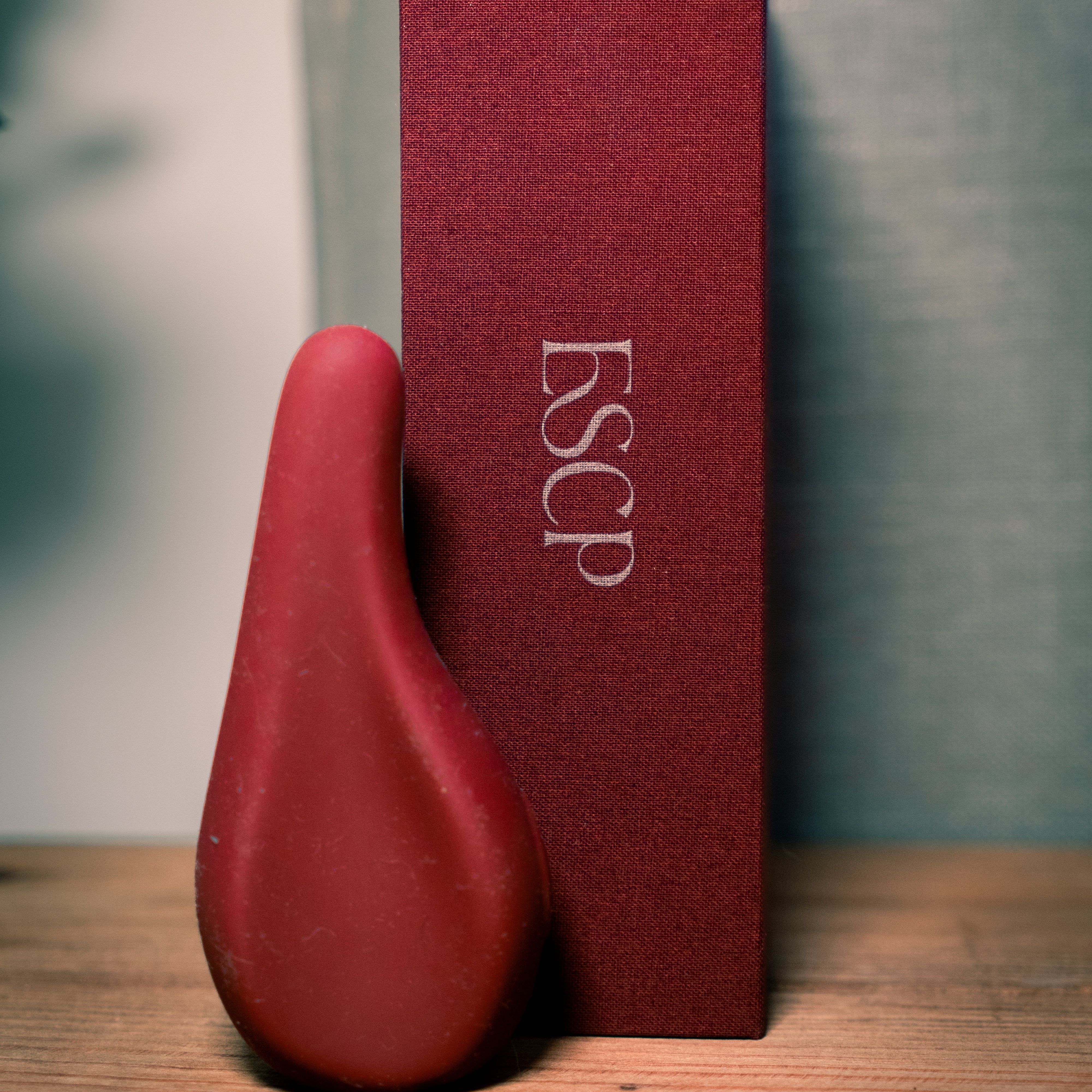 ESCP Wine coloured luxury silicone Clitoral massager with ergonomic design, shown with a branded box disguised as a book. discreet design.